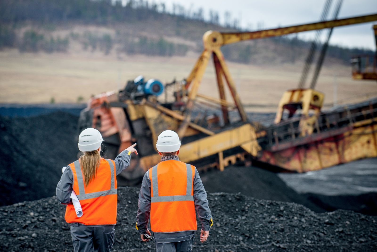 Two mining workers in safety vests and hard hats inspecting a bucket-wheel excavator at an open-pit coal mine