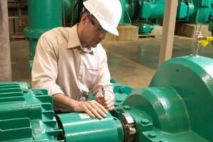 Chesterton field service technician in hard hat inspecting a pump and motor coupling assembly at an industrial facility