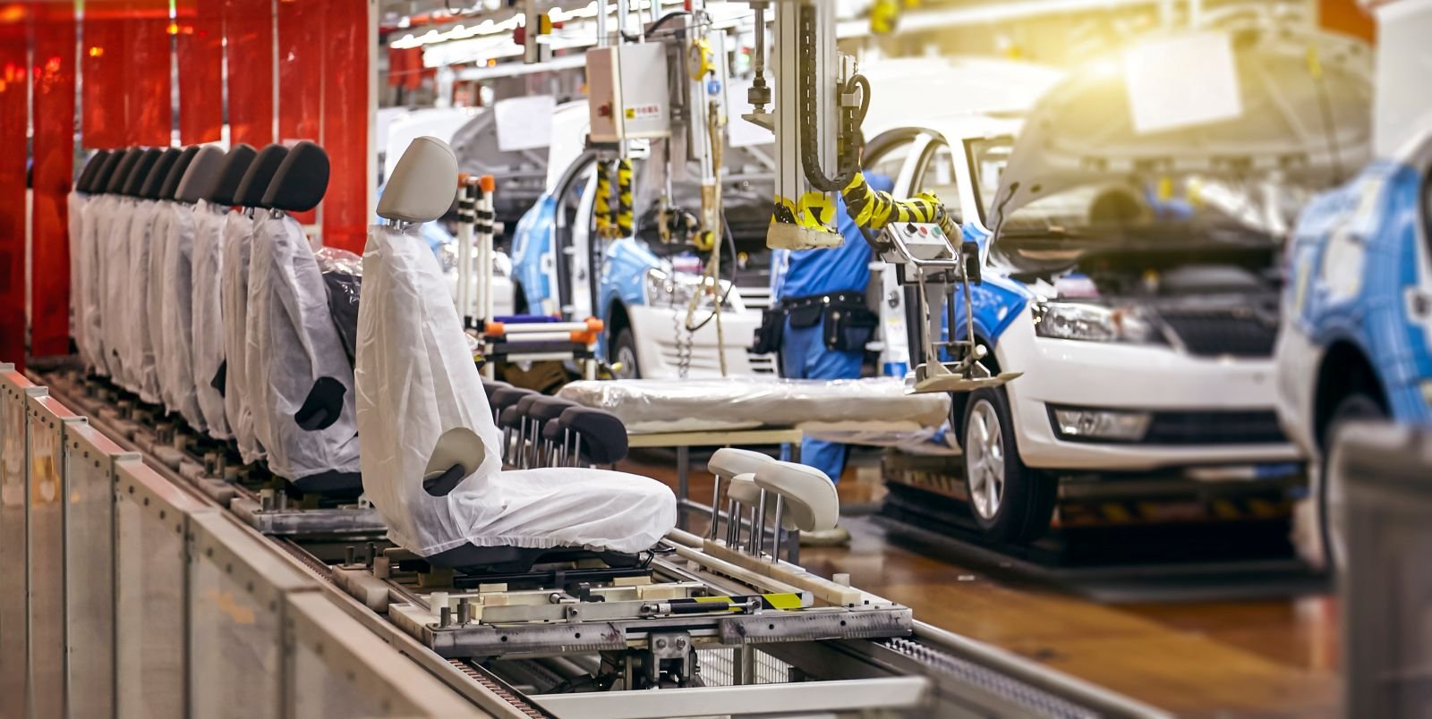 Linia montażowa w przemyśle motoryzacyjnym z fotelami samochodowymi na systemie przenośnikowym i ramionami robotycznymi pracującymi nad nadwoziami pojazdów w zakładzie produkcyjnym